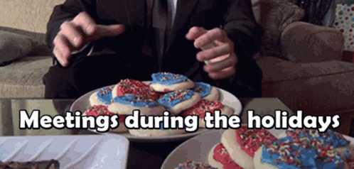 A Man In A Suit Is Sitting At A Table With A Plate Of Cookies And The Words Meetings During The Holidays Above Him GIF