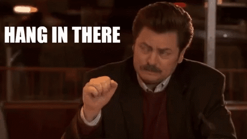 A Man In A Suit Is Sitting At A Table With His Fist In The Air And The Words `` Hang In There '' Behind Him . GIF