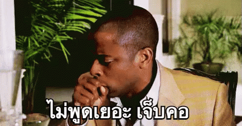 A Man In A Suit Is Sitting At A Table With His Hand In His Mouth And A Plant In The Background . GIF