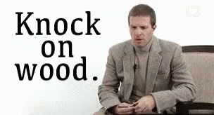 A Man In A Suit Is Sitting At A Table With The Words `` Knock On Wood '' . GIF