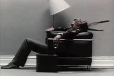 A Man In A Suit Is Sitting In A Black Chair GIF
