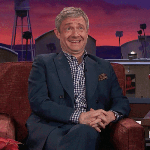 A Man In A Suit Is Sitting In A Chair And Laughing GIF