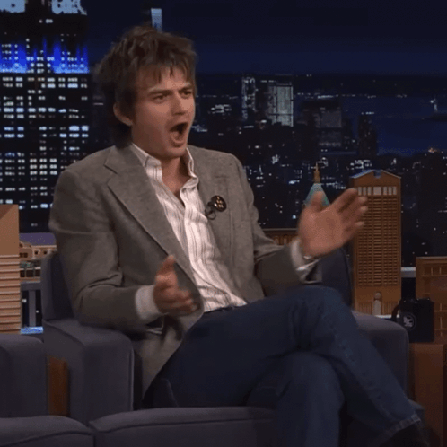 A Man In A Suit Is Sitting In A Chair And Making A Funny Face GIF