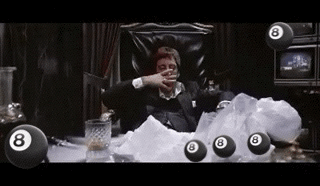 A Man In A Suit Is Sitting In A Chair Surrounded By Pool Balls . GIF