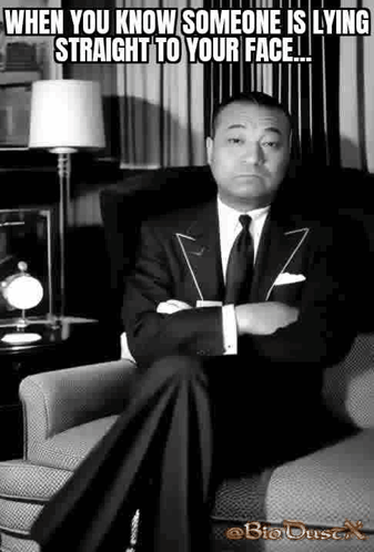A Man In A Suit Is Sitting In A Chair With His Arms Crossed . GIF