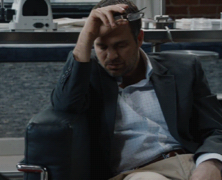 A Man In A Suit Is Sitting In A Chair With His Hand On His Forehead GIF