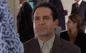 A Man In A Suit Is Sitting In A Crowd Of People GIF