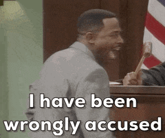 A Man In A Suit Is Sitting In Front Of A Judge Holding A Hammer . GIF