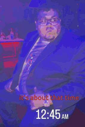 A Man In A Suit Is Sitting In Front Of A Sign That Says It 'S About That Time GIF