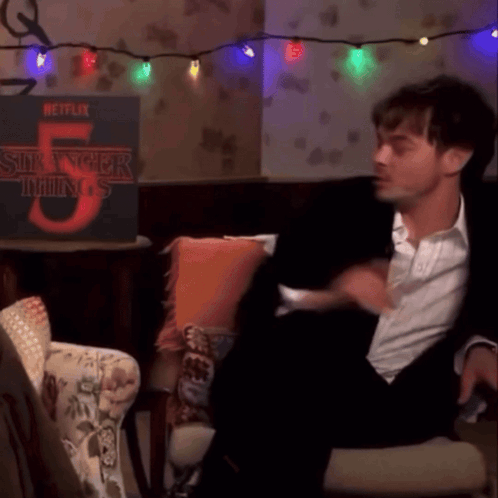 a man in a suit is sitting in front of a stranger things 5 poster