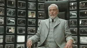 A Man In A Suit Is Sitting In Front Of A Wall Of Televisions . GIF