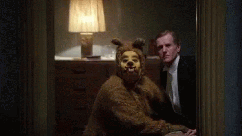 a man in a suit is sitting next to a bear costume .
