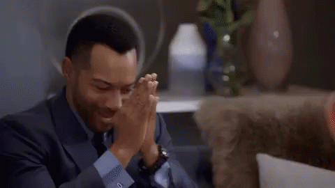 A Man In A Suit Is Sitting On A Couch And Adjusting His Sleeves . GIF