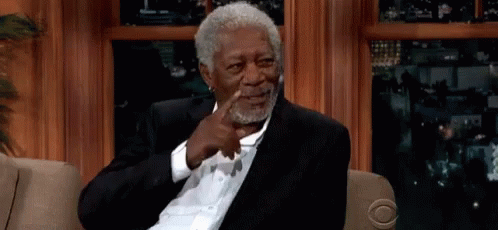 A Man In A Suit Is Sitting On A Couch And Pointing At Himself GIF