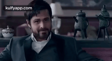 A Man In A Suit Is Sitting On A Couch In Front Of A Table With Teapots On It . GIF