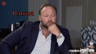 A Man In A Suit Is Sitting With His Hand On His Chin And The Word Patriot Is On The Screen GIF