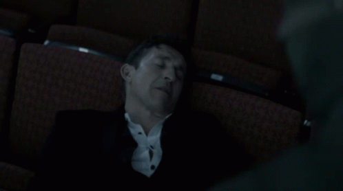 A Man In A Suit Is Sleeping In A Dark Auditorium Seat GIF