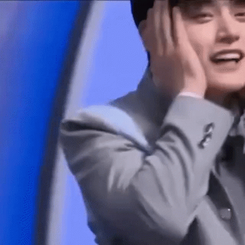 A Man In A Suit Is Smiling And Covering His Ears With His Hands . GIF
