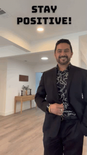 A Man In A Suit Is Smiling In Front Of A Sign That Says Stay Positive GIF