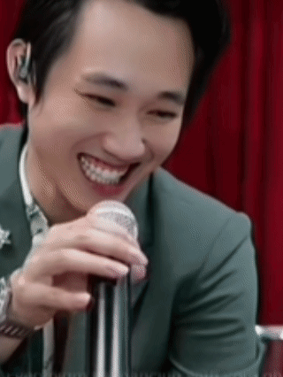 A Man In A Suit Is Smiling While Holding A Microphone In His Hand . GIF