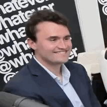 A Man In A Suit Is Smiling While Sitting In Front Of A Sign That Says `` What Do You Hate ? '' GIF
