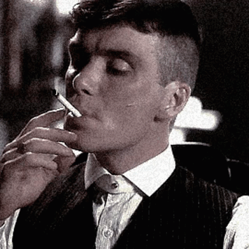 A Man In A Suit Is Smoking A Cigarette In A Black And White Photo . GIF