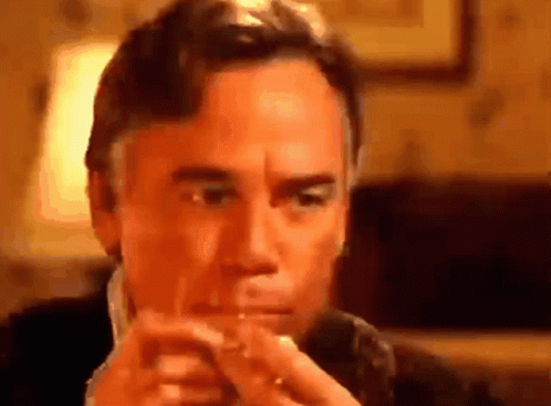 A Man In A Suit Is Smoking A Cigarette In A Room . GIF