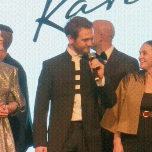 a man in a suit is speaking into a microphone while standing next to a woman