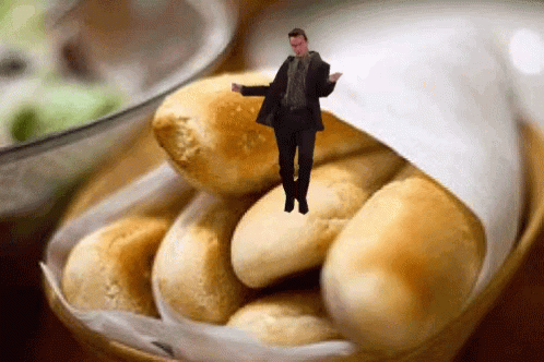 A Man In A Suit Is Standing In A Basket Of Bread GIF
