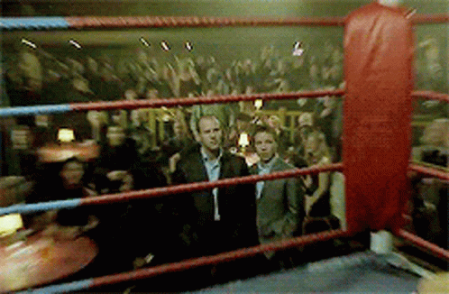 A Man In A Suit Is Standing In A Boxing Ring With A Crowd Behind Him GIF
