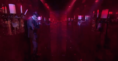 A Man In A Suit Is Standing In A Dark Room Holding A Candle . GIF