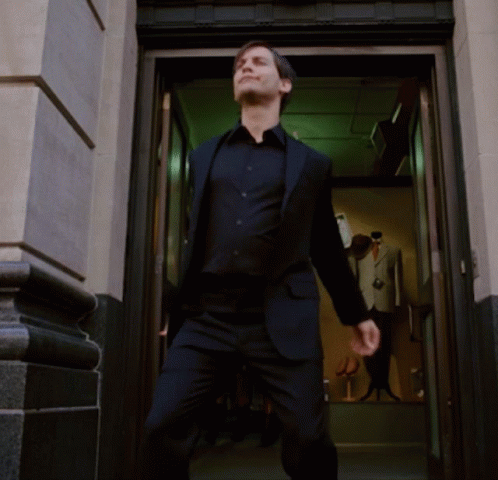 A Man In A Suit Is Standing In A Doorway With His Arms Outstretched GIF