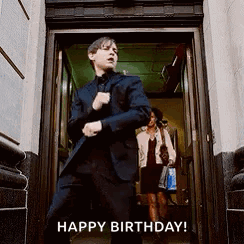 A Man In A Suit Is Standing In A Doorway With His Hands In His Pockets . GIF