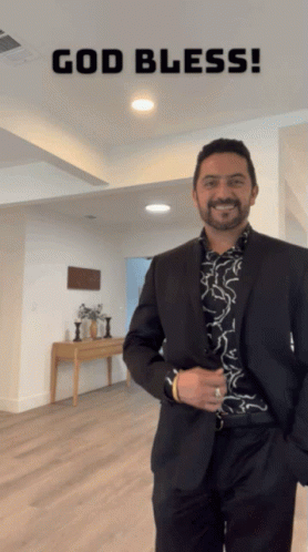 A Man In A Suit Is Standing In A Room With The Words God Bless Written Above Him GIF