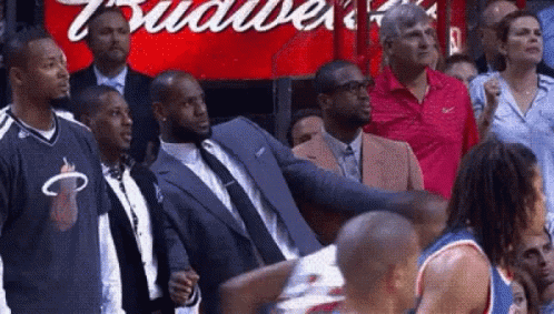 A Man In A Suit Is Standing In Front Of A Budweiser Sign . GIF