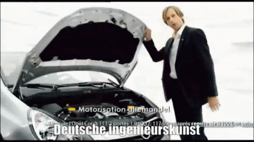 A Man In A Suit Is Standing In Front Of A Car With The Hood Open GIF
