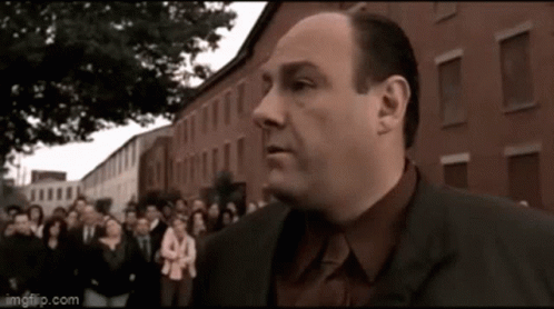 A Man In A Suit Is Standing In Front Of A Crowd Of People . GIF