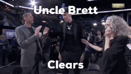 a man in a suit is standing in front of a crowd with the words uncle brett clears written above him .