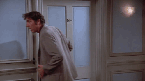 A Man In A Suit Is Standing In Front Of A Door That Says 5E GIF