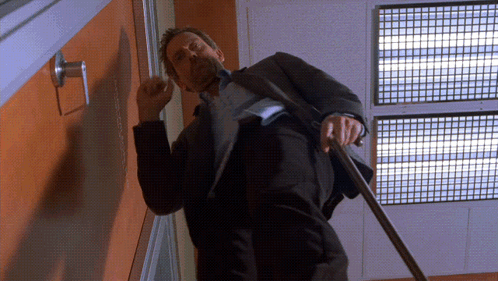 A Man In A Suit Is Standing In Front Of A Door With A Sign That Says ' Emergency Exit ' On It GIF