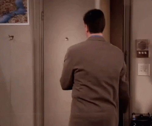 A Man In A Suit Is Standing In Front Of A Door With His Arms Crossed . GIF
