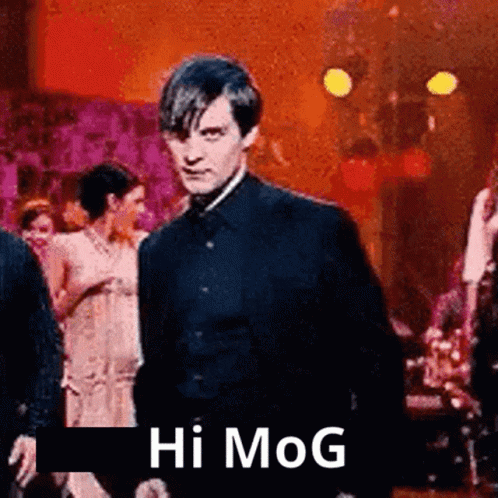 A Man In A Suit Is Standing In Front Of A Group Of People And Says Hi Mog . GIF