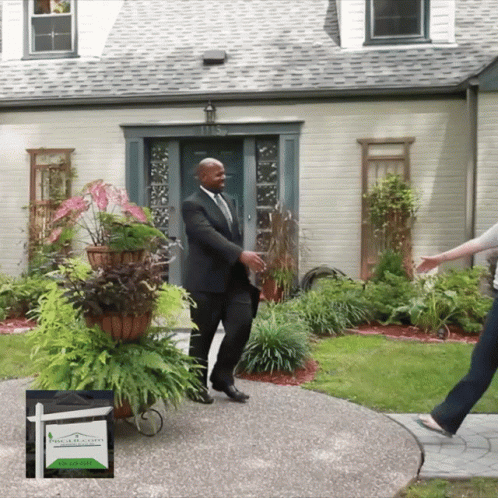 A Man In A Suit Is Standing In Front Of A House GIF