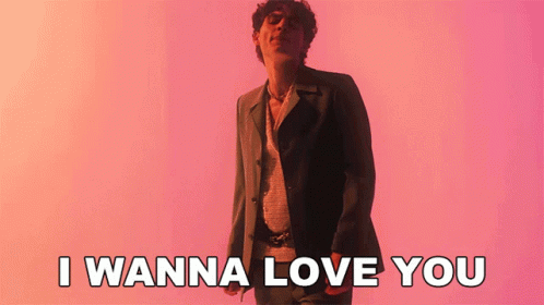 A Man In A Suit Is Standing In Front Of A Pink Background And Says I Wanna Love You GIF