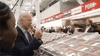 A Man In A Suit Is Standing In Front Of A Pork Section Of A Grocery Store GIF