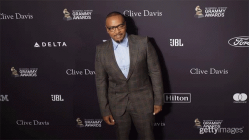 A Man In A Suit Is Standing In Front Of A Wall That Says Clive Davis On It GIF