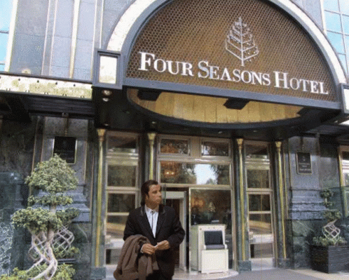 A Man In A Suit Is Standing In Front Of The Four Seasons Hotel GIF