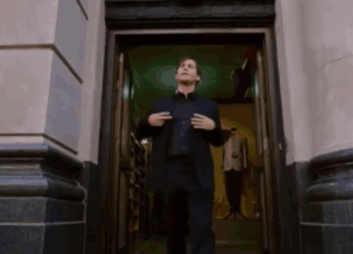A Man In A Suit Is Standing In The Doorway Of A Building GIF