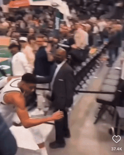 A Man In A Suit Is Standing Next To A Basketball Player In The Stands GIF