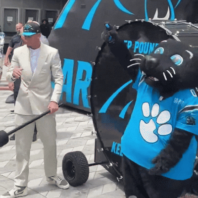 A Man In A Suit Is Standing Next To A Mascot Wearing A Blue Shirt That Says 50 On It GIF